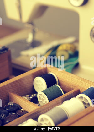Old vintage sewing utensils in a wooden box, sewing machine in background, retro film toned image Stock Photo