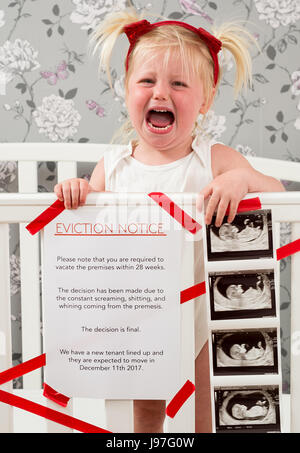 Funny baby announcement. A child stood up in the cot with a funny eviction notice on side. Stock Photo