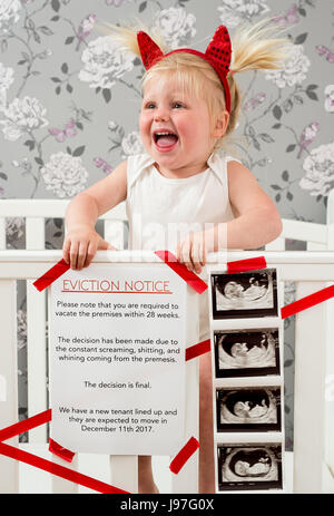 Funny baby announcement. A child stood up in the cot with a funny eviction notice on side. Stock Photo