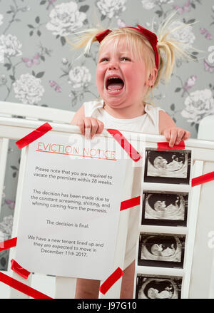 Funny baby announcement. A child stood up in the cot with a funny eviction notice on side. Stock Photo