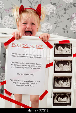 Funny baby announcement. A child stood up in the cot with a funny eviction notice on side. Stock Photo