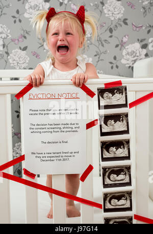 Funny baby announcement. A child stood up in the cot with a funny eviction notice on side. Stock Photo