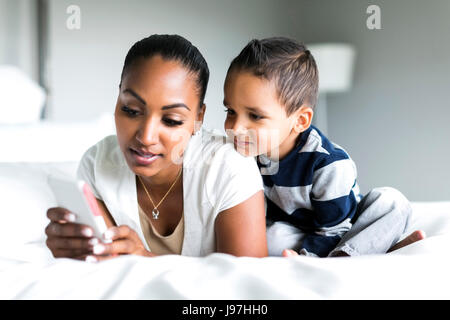 Mother and son (2-3) lying on bed and using smart phone Stock Photo
