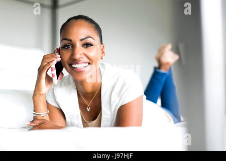 Smiling woman lying on bed and using phone Stock Photo