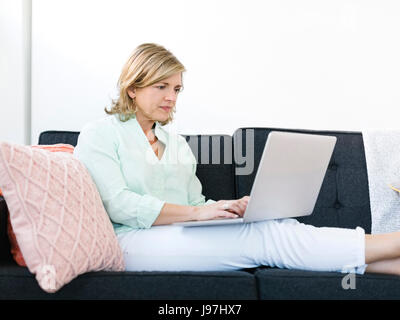 Woman sitting on sofa and using laptop Stock Photo