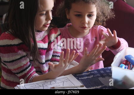 Young girl helping her sister solve addition problems by counting on her fingers Stock Photo