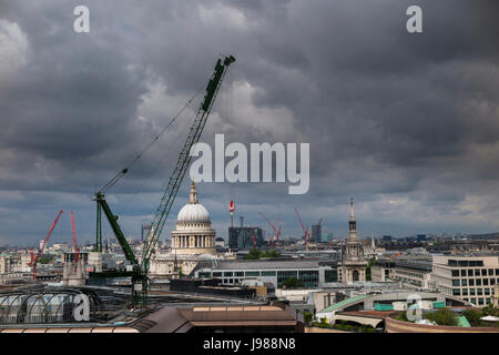 Tower cranes at the Bloomberg Place development site on the City of London skyline overlooking St Paul's Cathedral with grey gathering clouds Stock Photo