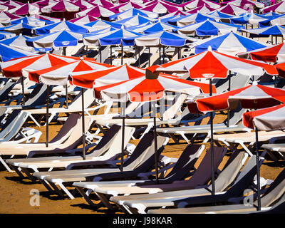 Rows of empty sun loungers and parasols on golden sandy beach Stock Photo