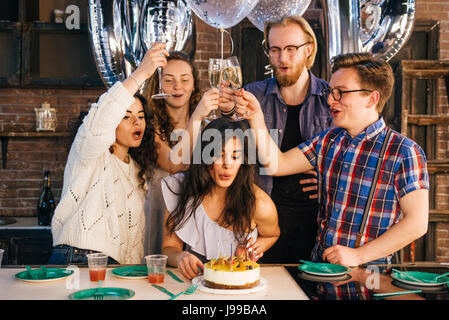 Young girl celebrates her birthday blowing out the candles with her friends Stock Photo