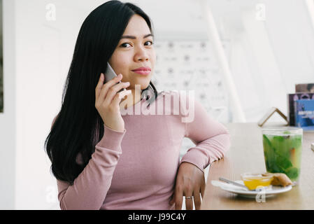 Young asiatic look girl drink green fresh tea and talking to friend on mobile phone Stock Photo
