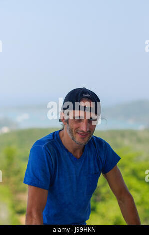 a happy Young Bearded Man sitting on the stone railings in city park wearing in blank blue t-shirt and black Cap Stock Photo