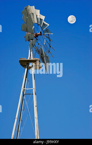 A Kansas prairie windmill stands tall and proud against deep blue sky and full moon Stock Photo