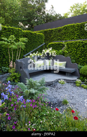 A seating area made from concrete surrounded by plants including Rosa 'Rambling Rector and a high hedge in the Linklaters Garden for Maggie's at the R Stock Photo