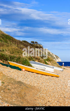 Four boats on the shingle beach at Ringstead Bay, Dorset, England, UK, a single figure in the background Stock Photo