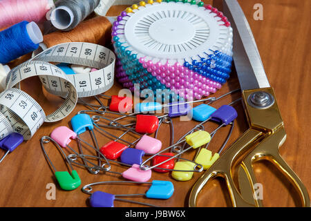 Greater sewing scissors, color a thread, a measuring tape and pins on a table Stock Photo