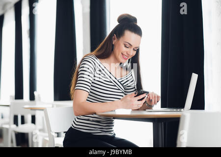 Smiling attractive woman reading text message on mobile phone at restaurant. Stock Photo