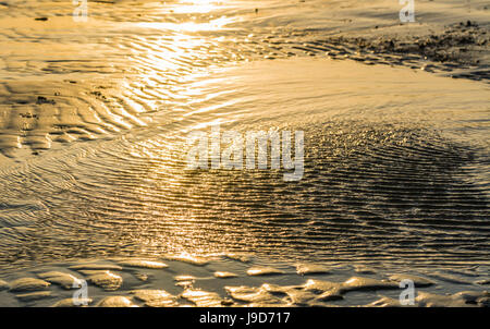 Ripples of water at low tide on a sandy beach with sunlight reflecting in the sea water. Stock Photo