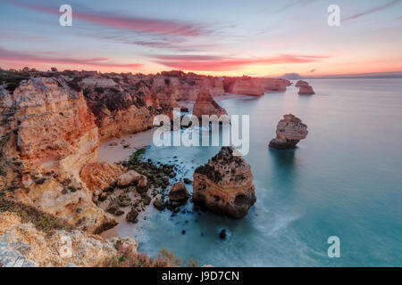Sunrise on cliffs framed by turquoise water of the ocean, Praia da Marinha, Caramujeira, Lagoa Municipality, Algarve, Portugal Stock Photo