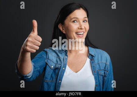 Nice work. Inspiring positive gorgeous woman supporting someones statements by using an approving gesture while standing isolated on grey background Stock Photo