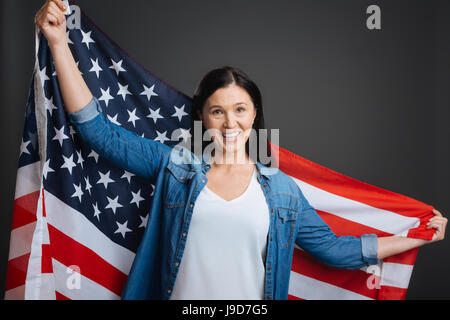 Holding it high and proud. Gorgeous inspirational pretty lady celebrating Independence Day and holding up the national flag while standing isolated on Stock Photo