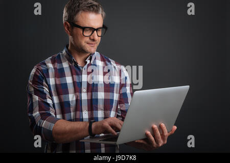 Working from anywhere. Focused motivated handsome guy writing an email while using his laptop and wearing the glasses Stock Photo