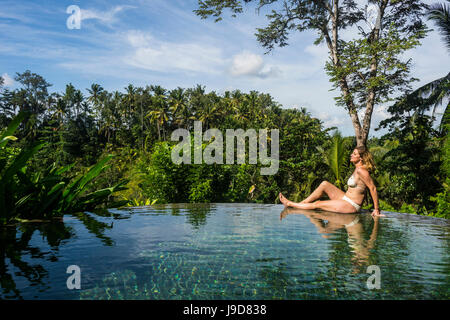 Woman enjoying an overflowing pool above a valley in the Kamandalu Ubud resort, Ubud, Bali, Indonesia, Southeast Asia, Asia Stock Photo