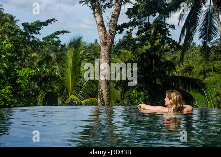 Woman enjoying an overflowing pool above a valley in the Kamandalu Ubud resort, Ubud, Bali, Indonesia, Southeast Asia, Asia Stock Photo