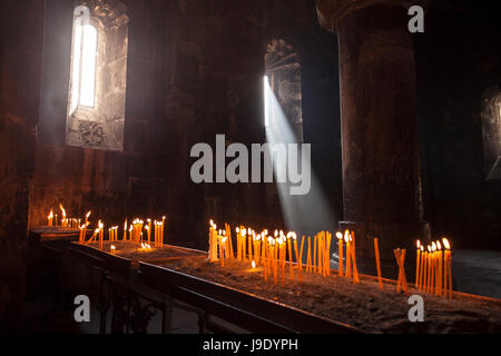 Candles in Medieval Armenian christian church interior with sun rays from the window falling on the candles. Religion, architecture, travel concept. Stock Photo