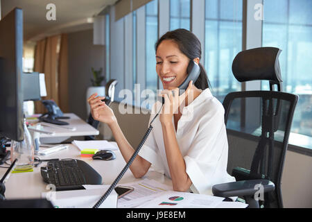 Businesswoman Making Phone Call Sitting At Desk In Office Stock Photo