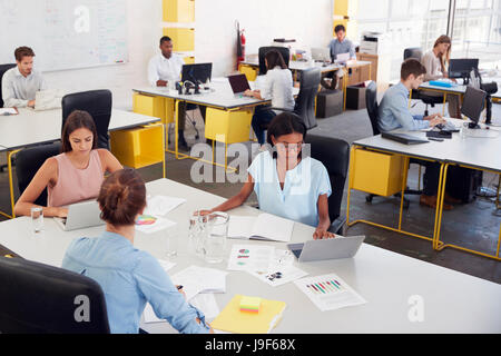 Three women share a desk in a busy office, elevated view Stock Photo
