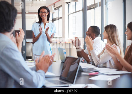 Young black woman stands clapping with colleagues at meeting Stock Photo
