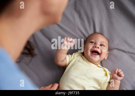 Mother Playing With Newborn Baby Son Lying On Bed In Nursery Stock Photo