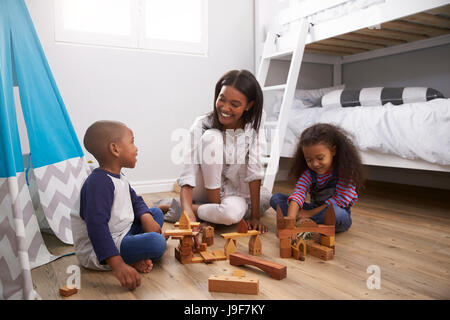 Mother And Children Playing With Building Blocks In Bedroom Stock Photo