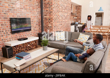 Father And Son Sit On Sofa In Lounge Watching Television Stock Photo