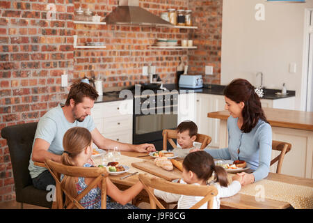 Family Praying Before Eating Meal In Kitchen Together Stock Photo