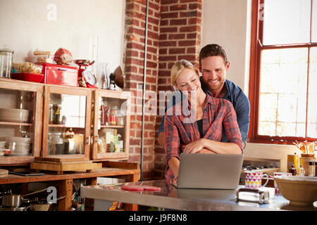 Young white couple using laptop in kitchen embracing Stock Photo