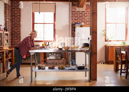 Young woman using computer in kitchen, full length side view Stock Photo