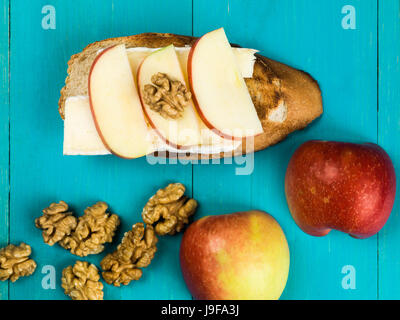 Sliced Apple with Brie Cheese and Walnuts on Toasted Baguette Against a Blue Background Stock Photo