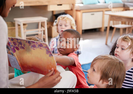 Pupils At Montessori School Looking At Book With Teacher Stock Photo