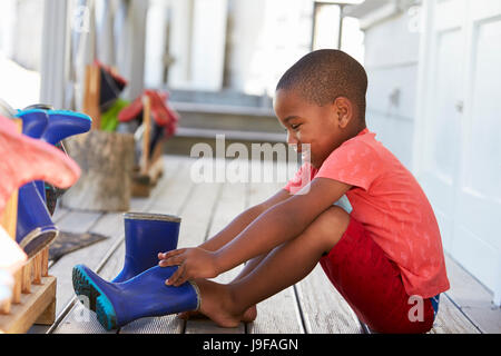 Male Pupil At Montessori School Putting On Wellington Boots Stock Photo