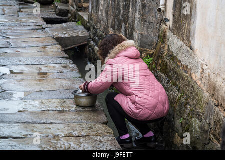 Woman washing saucepan in waterway in the street, Ancient Hongcun Village, Huangshan, Anhui province, China Stock Photo