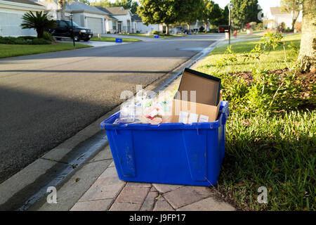 A blue coloured recycling box containg plastics and paper products on the sidewalk of a residential housing estate in Florida USA Stock Photo