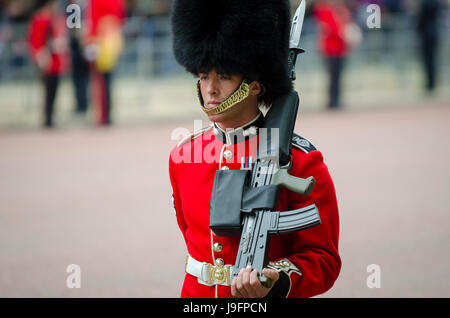 LONDON - JUNE 13, 2015: Royal guard in traditional red coat and bear fur busby hat stands on the Mall with rifle in a Trooping the Colour celebration. Stock Photo