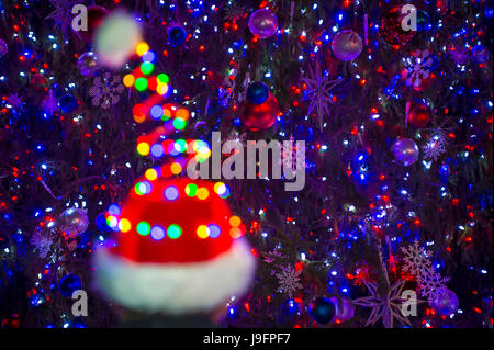Colorful holiday lights glow on a Santa hat in front of a twinkling Christmas tree background Stock Photo