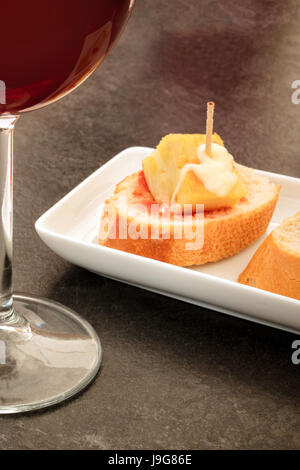 Spanish tapas in a bar. A glass of red wine and pinchos of tortilla, Spanish omelette, on slices of bread. On a dark black table with a place for text Stock Photo