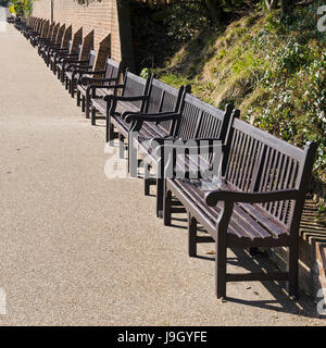 Long row of empty wooden bench seats along Eastbourne promenade on a sunny spring day, Eastbourne, East Sussex, England, UK Stock Photo