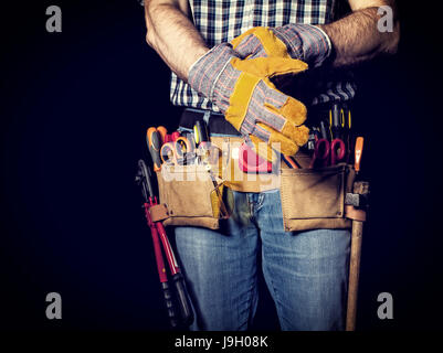 detail of handyman with leather toolsbelt and tools on dark background wearing gloves Stock Photo