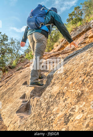 Male hiker climbing a steep trail of Ute Canyon in Colorado National Monument, morning spring scenery Stock Photo