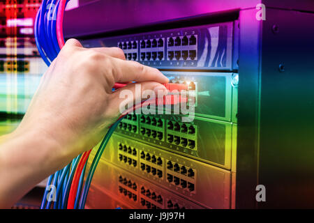 man working in network server room with fiber optic hub for digital communications and internet Stock Photo