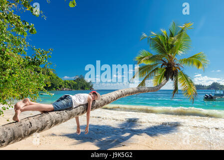 Cute boy resting lying on a palm tree at tropical island on vacationю
